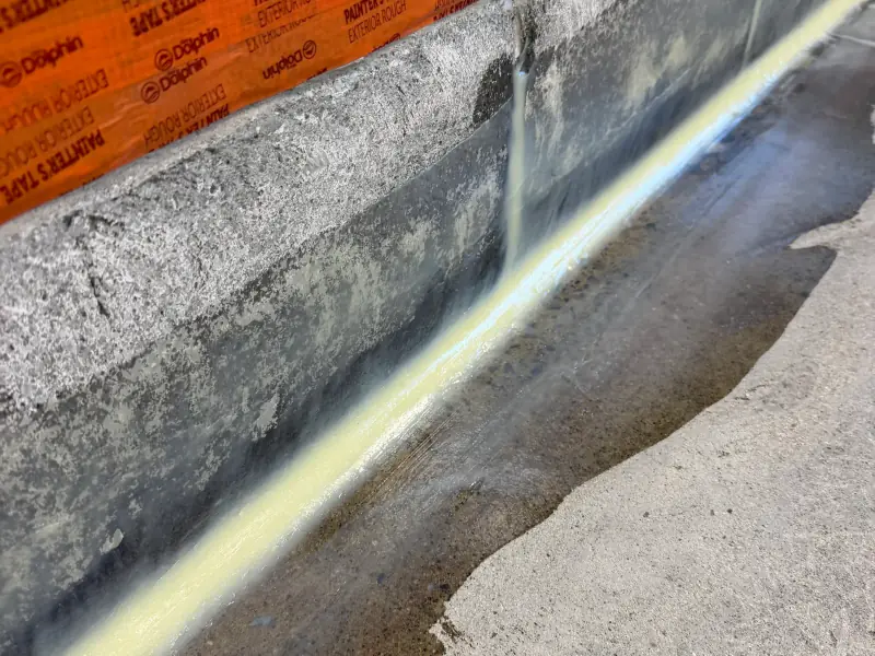 Cordon de scellant à la jonction mur-plancher d’un mur de fondation, ruban de masquage au-dessus, avant l’application